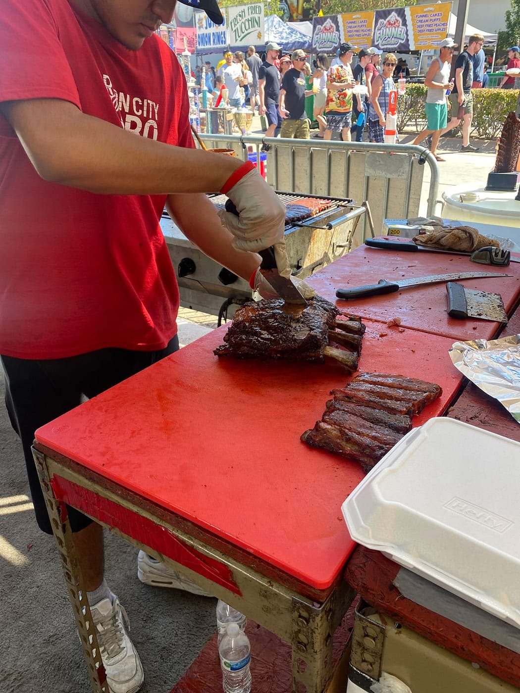 A crew member in a red Carson City BBQ shirt trimming racks of ribs on a red prep table at the Nugget rib cook-off.