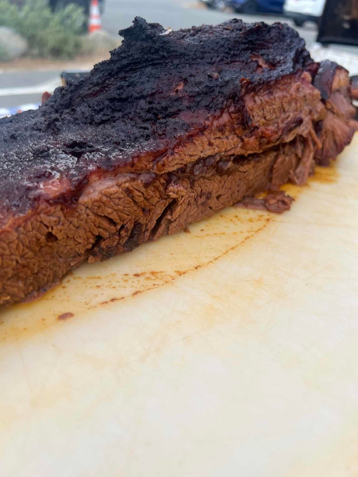 A whole smoked beef brisket with a thick black pepper bark, resting on a cutting board before slicing.