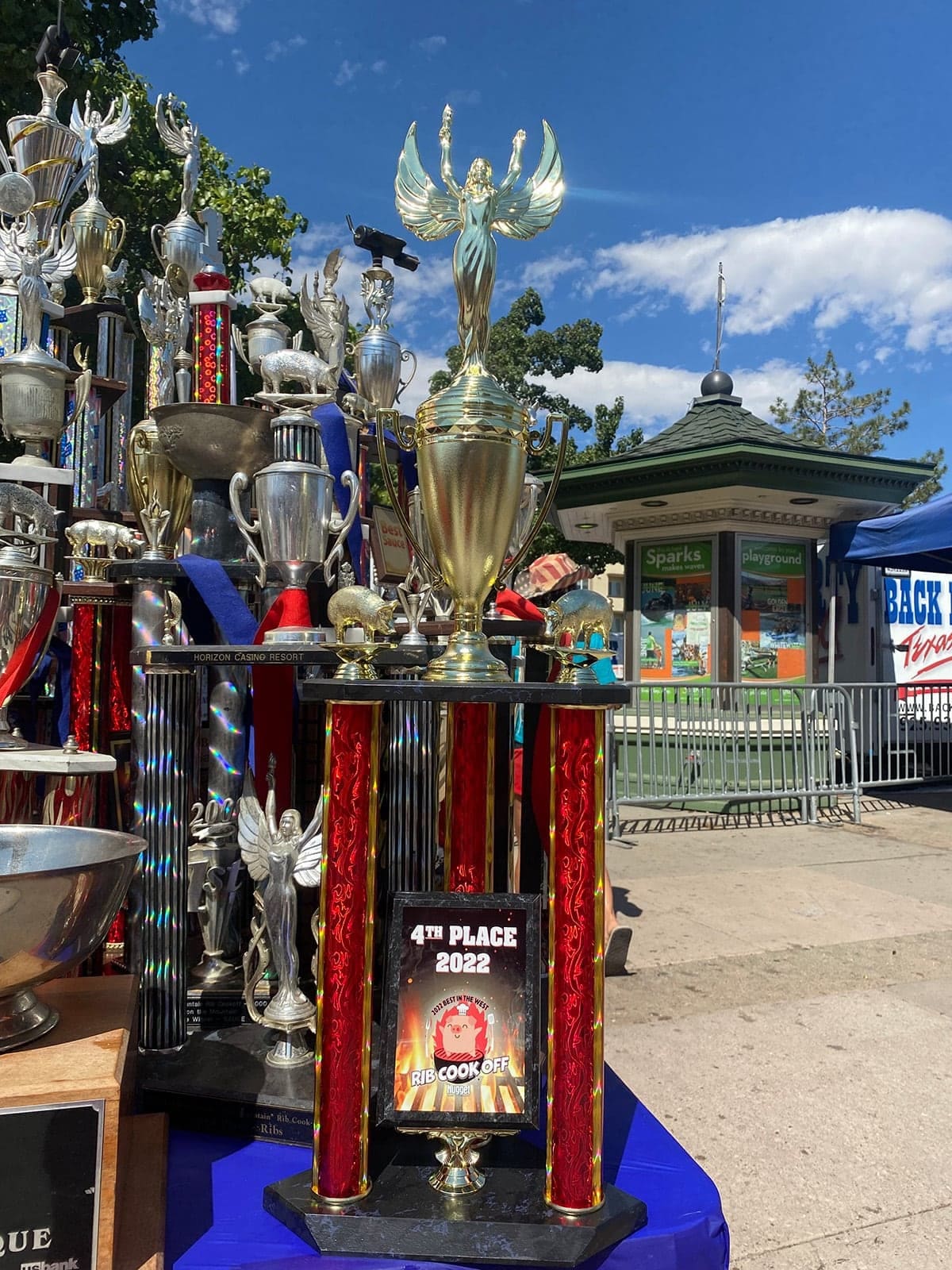 A tall silver-and-red trophy topped with flame-shaped ornaments, its plaque reading "4th Place 2022", standing outdoors at a cook-off.