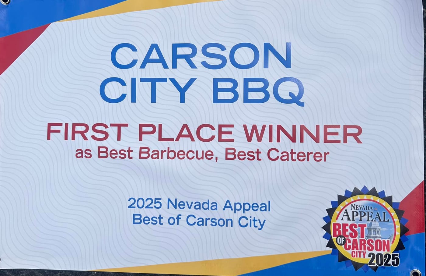 A printed banner reading "Carson City BBQ — First Place Winner as Best Barbecue, Best Caterer, 2025 Nevada Appeal Best of Carson City", with the Nevada Appeal Best of Carson City 2025 rosette.