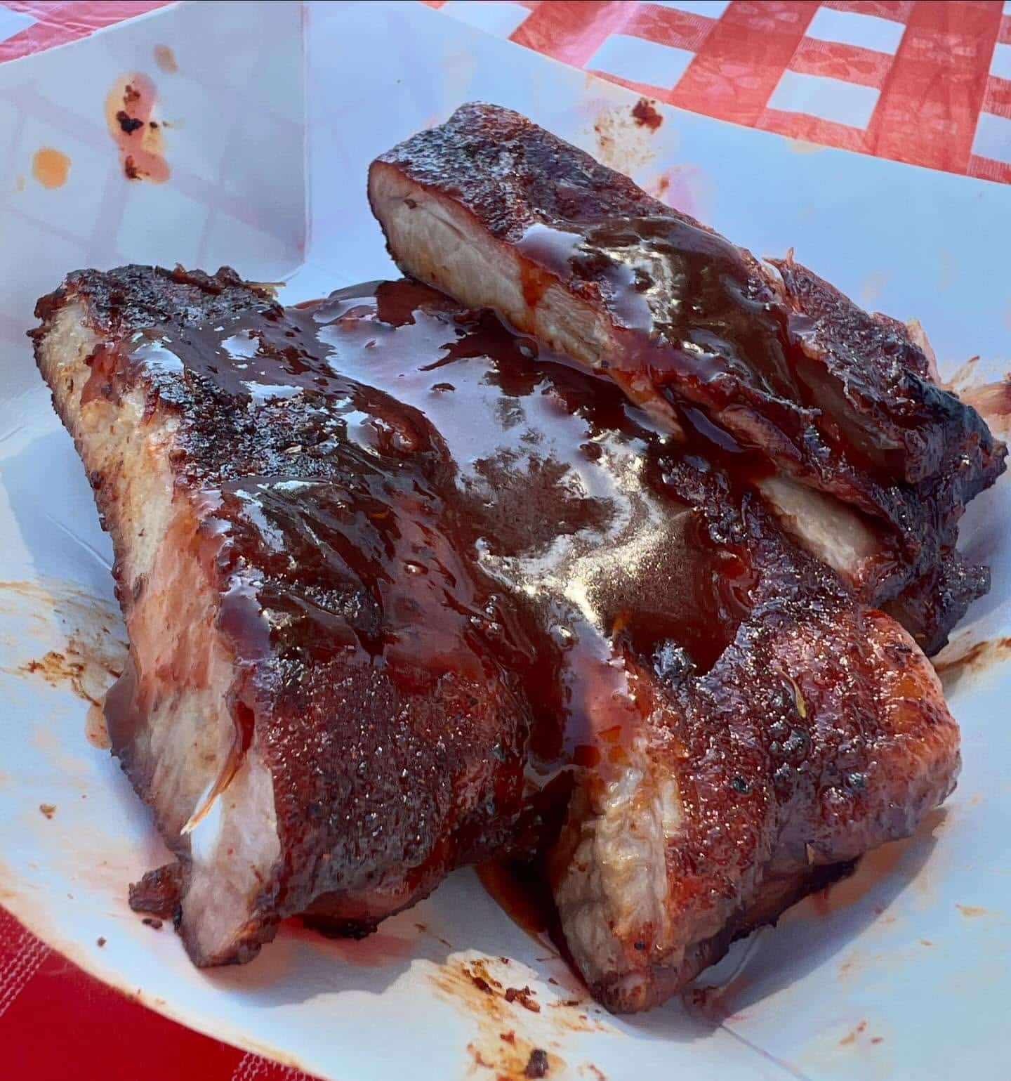 A close-up of a plate of glazed pork ribs, sauce pooling on the plate beneath them.