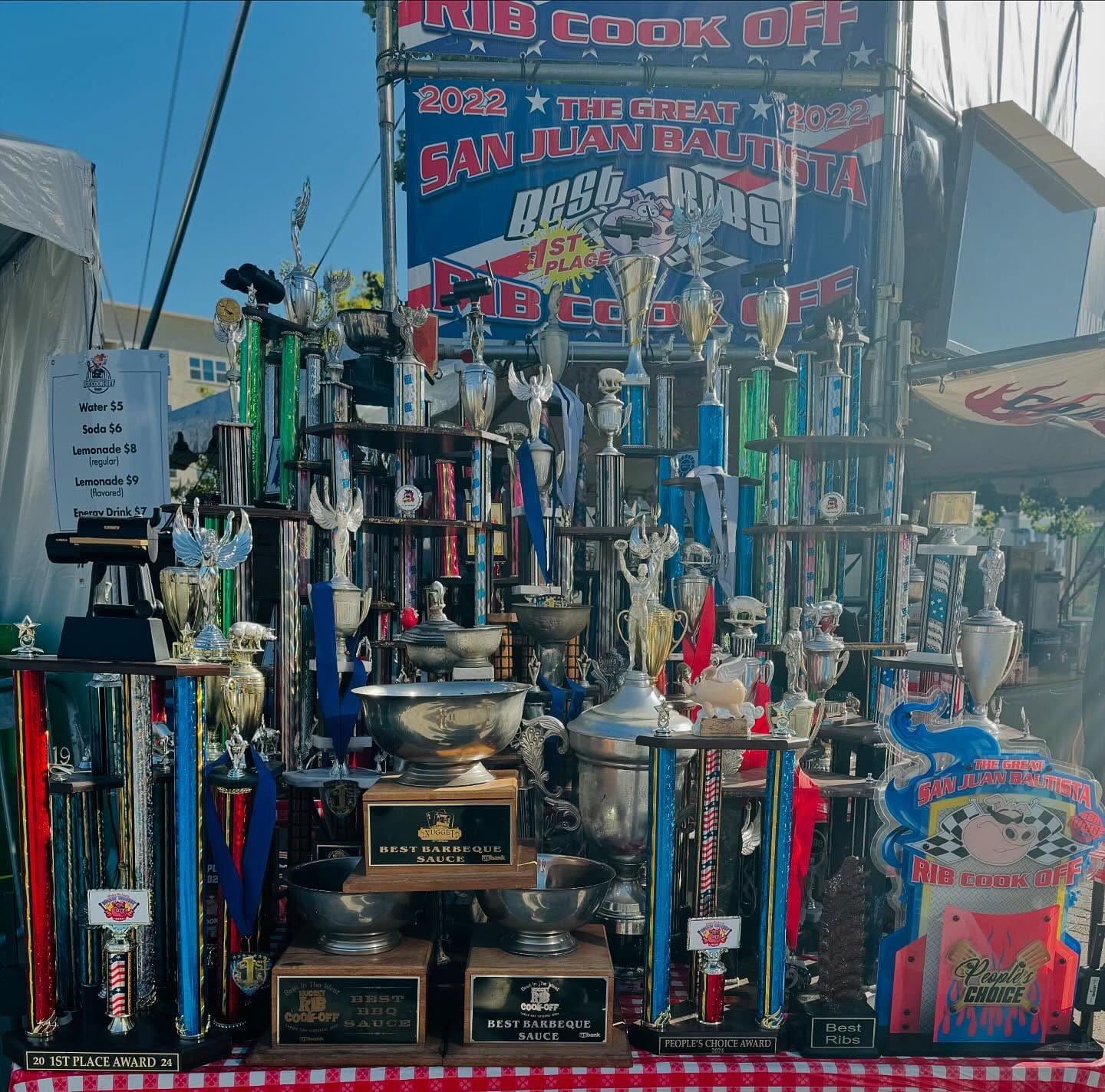 Dozens of trophies and plaques crowded together on tables beneath the team's San Juan Bautista rib cook-off booth signage.