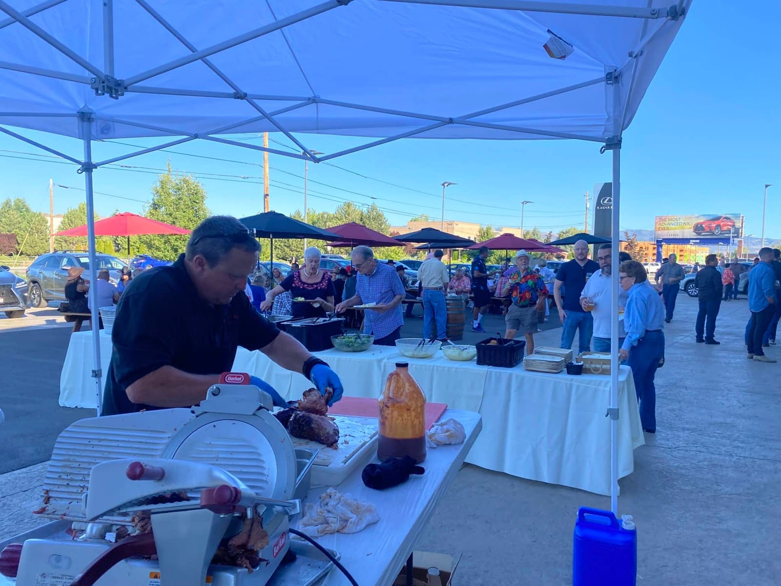A Carson City BBQ crew member slicing meat at a white-clothed prep table under a canopy, with a busy outdoor event crowd behind.