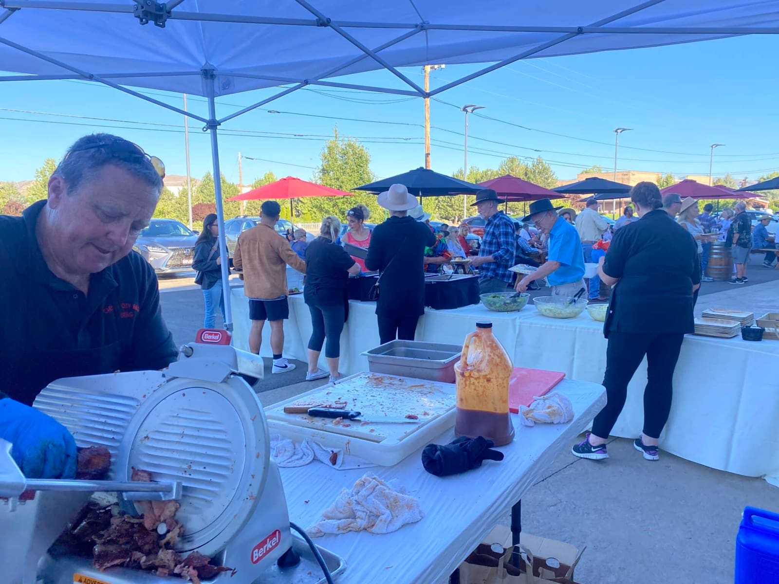 A smiling crew member working the slicer at the outdoor prep station, bottles of Carson City BBQ sauce lined up along the table.