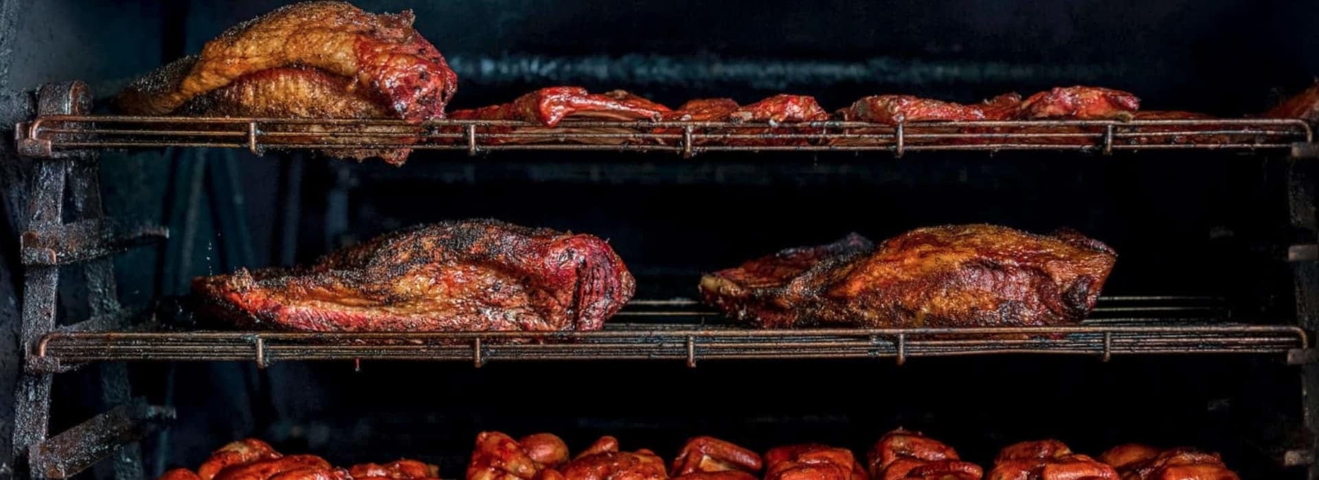 Smoked brisket and chicken resting across the stacked wire shelves of the smoker, dark-crusted and glistening.